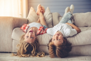 Zwei Geschwister liegen fröhlich auf der Couch und lauschen unseren Blogartikeln