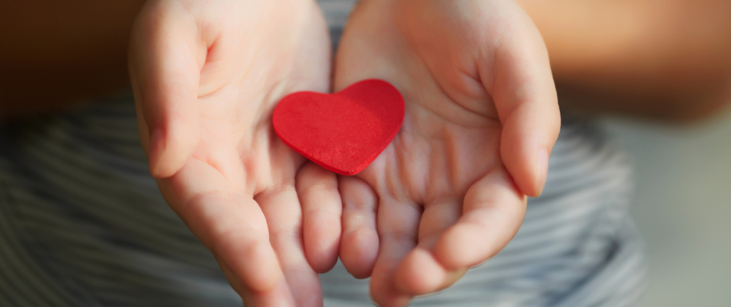 Ein Mädchen hält behutsam ein rotes Herz aus Filz in den Händen und heisst Sie herzlich willkommen